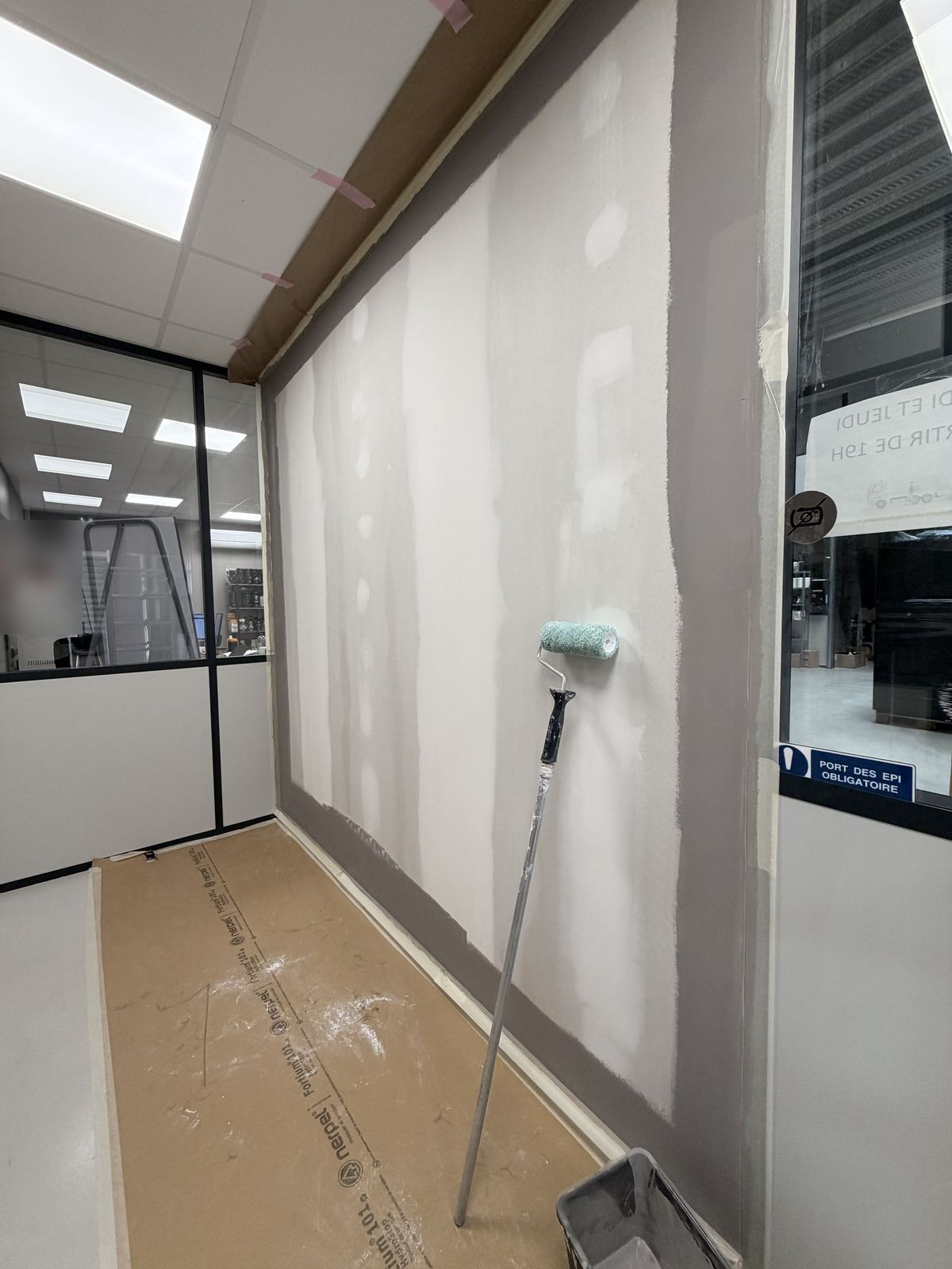 Mise en peinture en cours, bords déjà peints en taupe, rouleau posé contre le mur